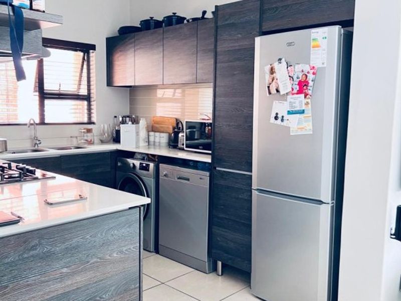 Modern kitchen featuring dark wood-grain cabinetry, stone countertops, tiled flooring, and integrated appliances including a dishwasher and hob.
