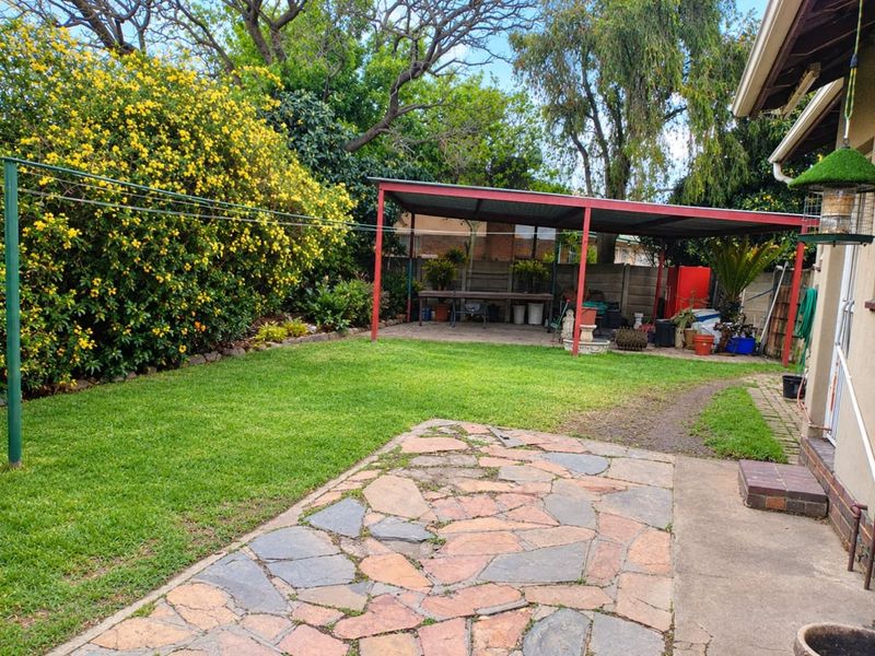 Rear garden featuring a lawn, paved patio area, and a covered carport structure with established perimeter landscaping.