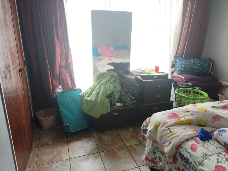 A bedroom featuring tiled flooring and a built-in cupboard, currently cluttered with personal belongings.