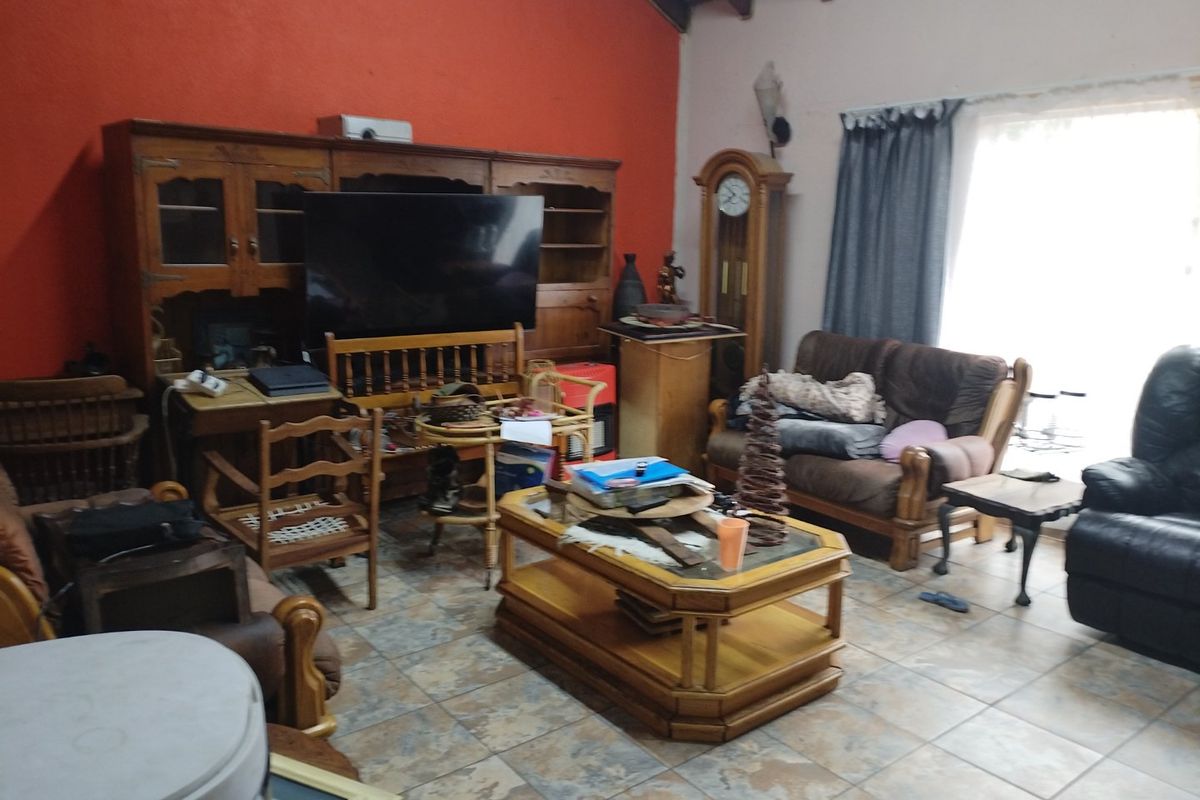 A living room featuring exposed timber ceiling beams and tiled flooring, offering a spacious layout with potential for modern updates.
