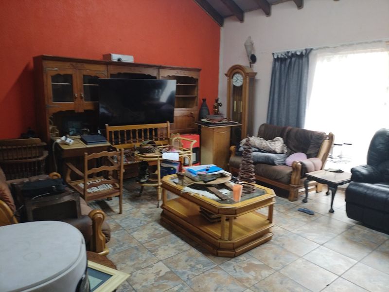 A living room featuring exposed timber ceiling beams and tiled flooring, offering a spacious layout with potential for modern updates.