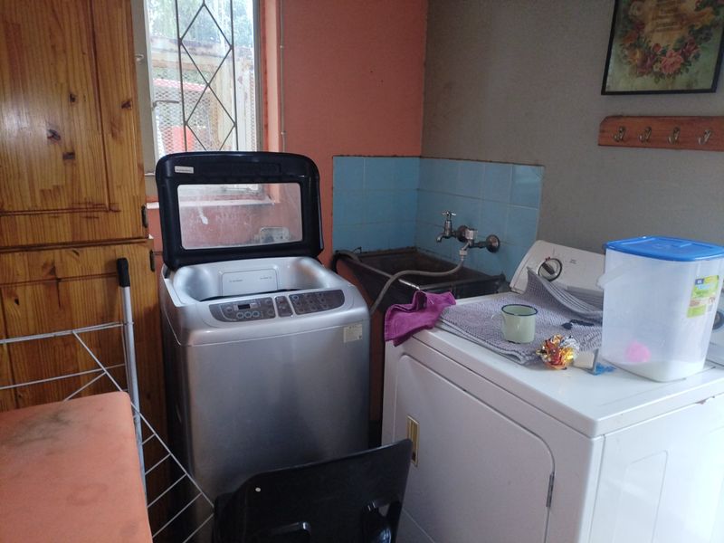 A functional laundry room featuring a built-in sink, tiled splashback, and integrated wooden cabinetry, providing essential utility space for the home.