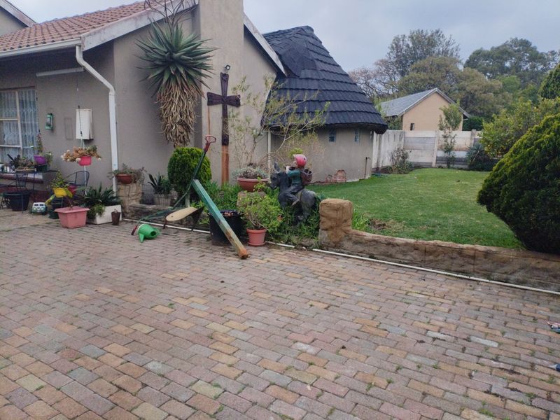 Rear exterior view of the property featuring a paved driveway, stone retaining wall, and a combination of tiled and thatched roof sections.