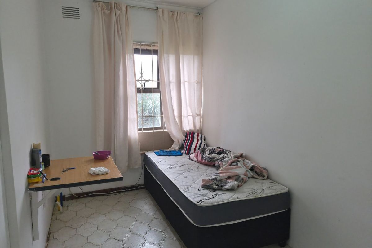 A compact bedroom featuring a wall-mounted desk, security bars on the window, and tiled flooring, offering a functional space for a single occupant.