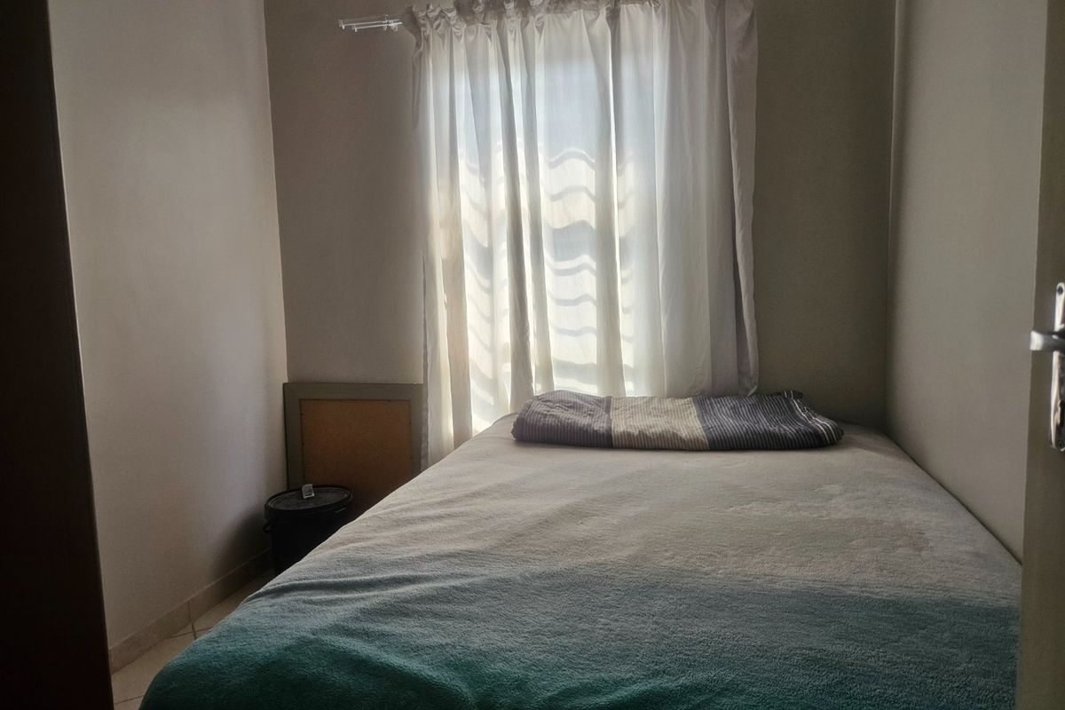 A compact bedroom featuring tiled flooring and a window with a curtain rod, providing a functional space for a single bed.