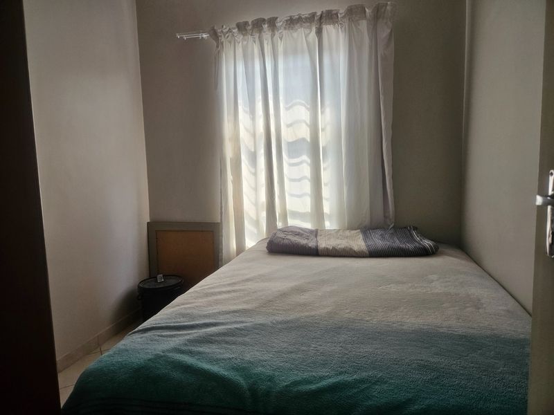 A compact bedroom featuring tiled flooring and a window with a curtain rod, providing a functional space for a single bed.