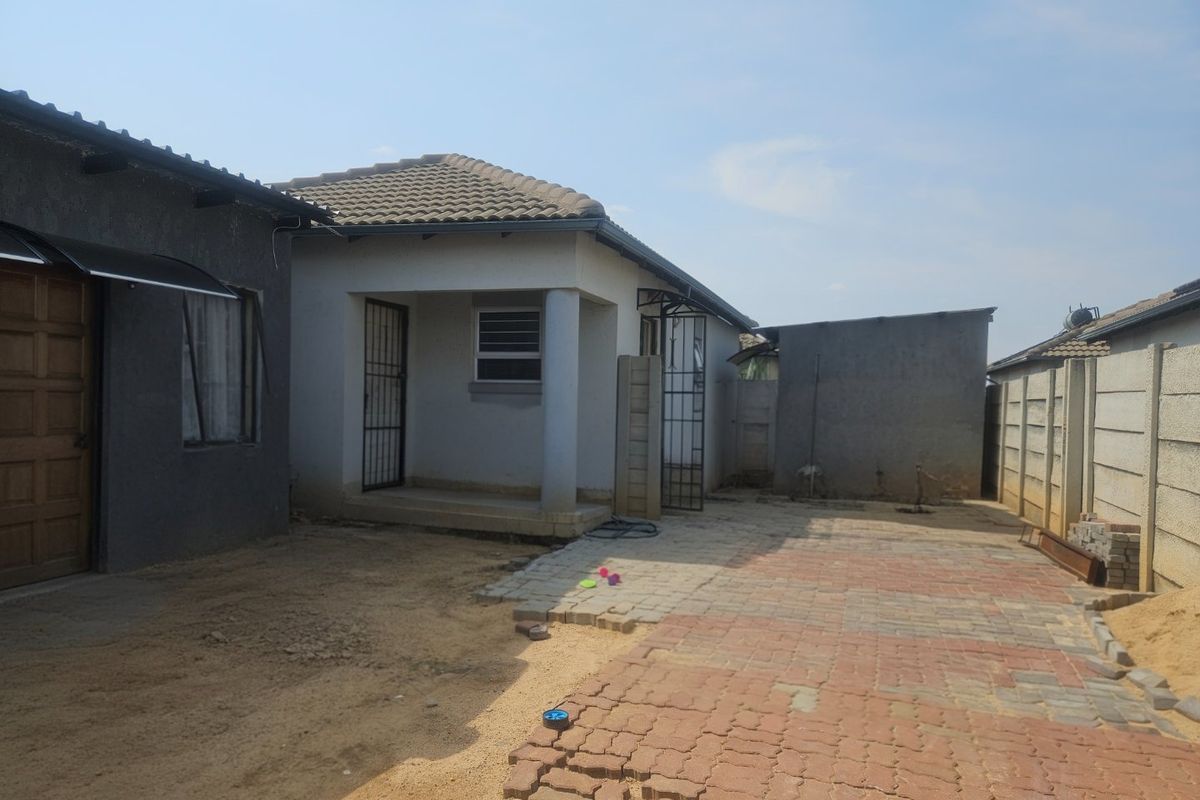 Rear exterior view of the house featuring a covered patio, concrete paved area, and perimeter precast walling with some unfinished landscaping.
