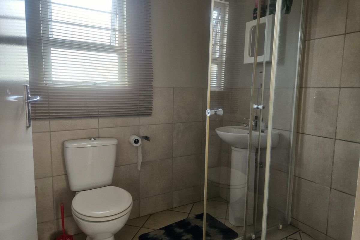 A functional bathroom featuring a pedestal basin, a glass-enclosed shower, and neutral wall and floor tiling with natural light from the window.