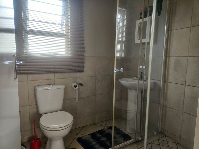 A functional bathroom featuring a pedestal basin, a glass-enclosed shower, and neutral wall and floor tiling with natural light from the window.