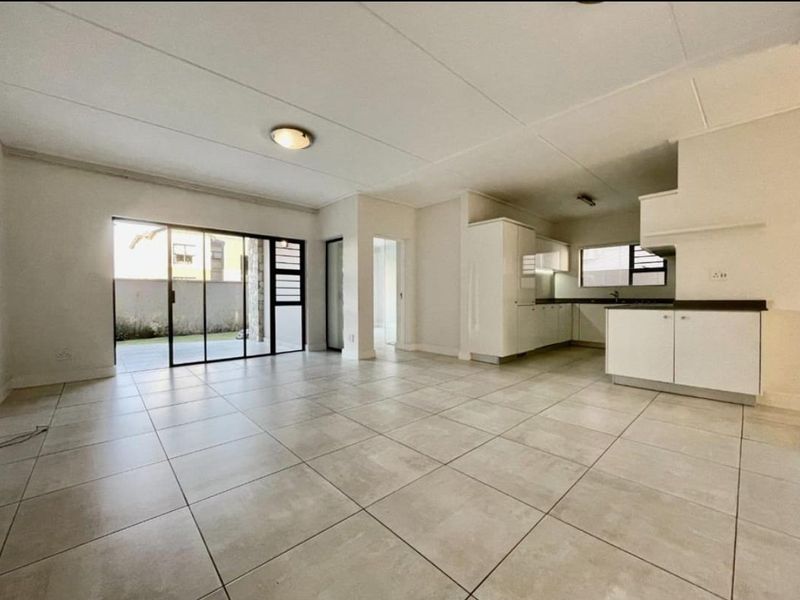Spacious open-plan living and kitchen area featuring neutral tiled flooring, modern cabinetry, and large sliding glass doors leading to an outdoor space.