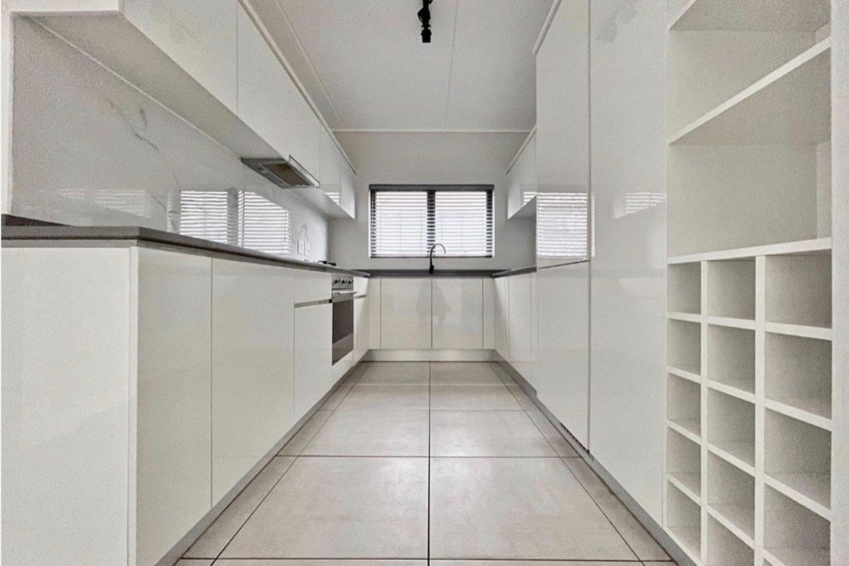 A modern, minimalist galley kitchen featuring high-gloss white cabinetry, stone countertops, integrated appliances, and sleek tiled flooring.