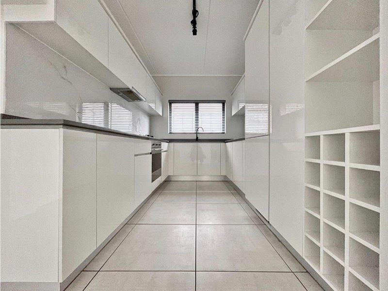 A modern, minimalist galley kitchen featuring high-gloss white cabinetry, stone countertops, integrated appliances, and sleek tiled flooring.