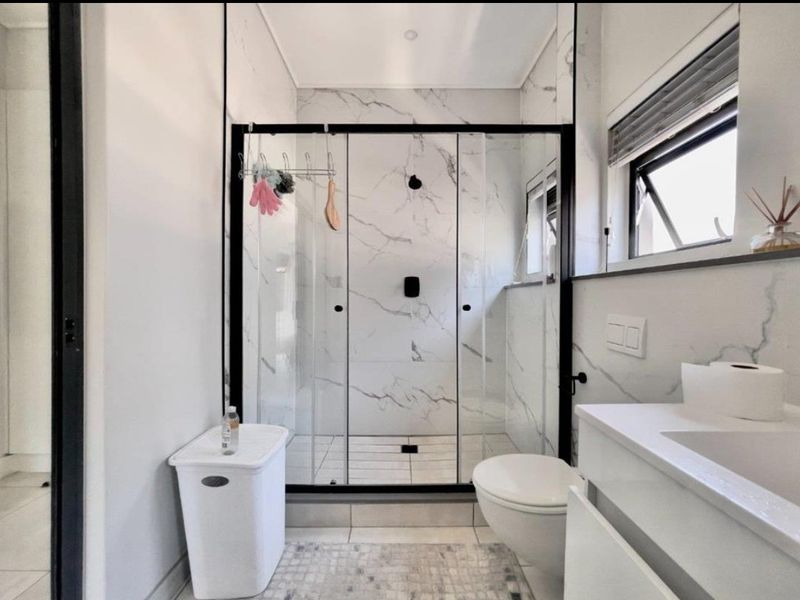 Modern bathroom featuring a walk-in shower with black-framed glass enclosure, marble-look wall tiles, wall-mounted toilet, and a sleek vanity basin.