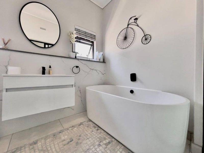 Modern bathroom featuring a sleek freestanding bathtub, wall-mounted vanity, and elegant marble-look wall tiles with contemporary black fixtures.