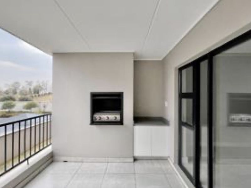 A modern covered balcony featuring tiled flooring, a built-in braai, storage cabinetry, and a metal balustrade with views.