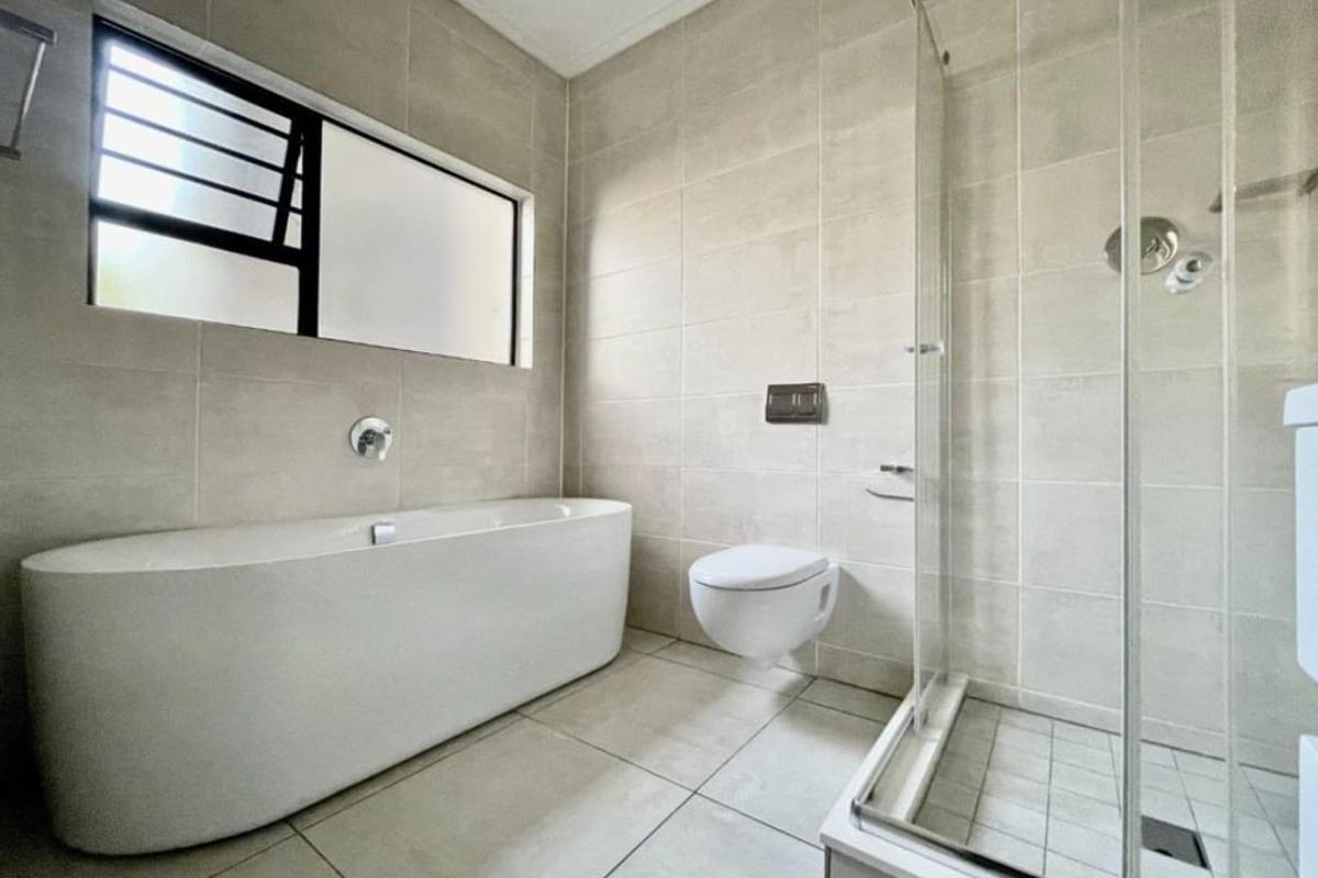 Modern bathroom featuring a freestanding bathtub, wall-mounted toilet, and a separate glass-enclosed shower with neutral floor-to-ceiling tiling.