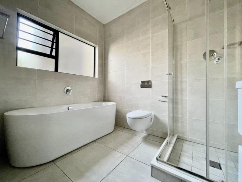 Modern bathroom featuring a freestanding bathtub, wall-mounted toilet, and a separate glass-enclosed shower with neutral floor-to-ceiling tiling.