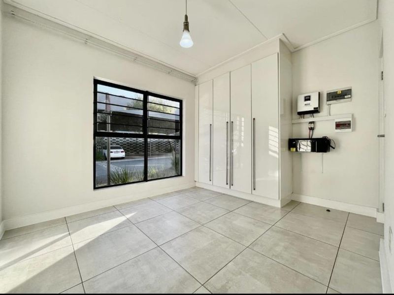 A bright, empty bedroom featuring modern tiled flooring, built-in cupboards, and a wall-mounted inverter system for backup power.