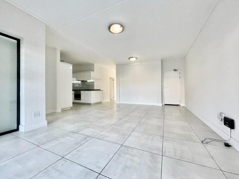 A bright, open-plan living and kitchen area featuring neutral tiled flooring, modern white cabinetry, and clean finishes throughout.