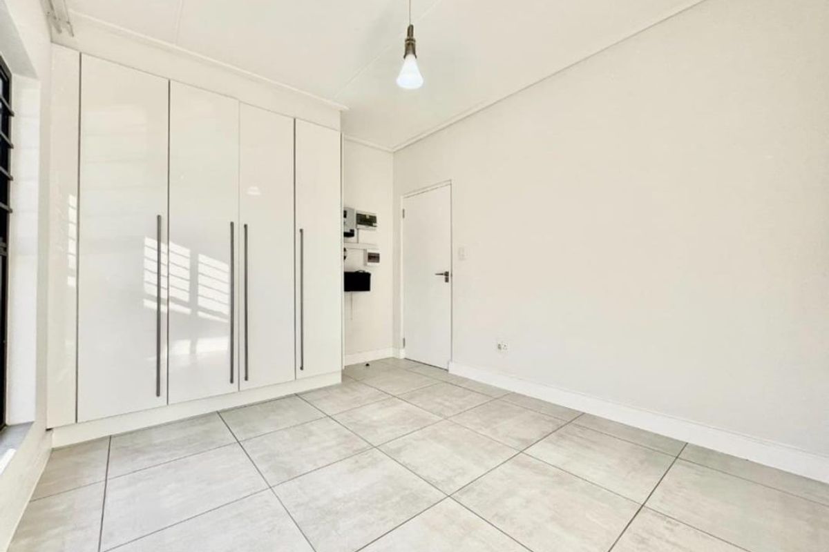 A bright, empty bedroom featuring modern large-format floor tiles and floor-to-ceiling built-in cupboards with a clean, minimalist aesthetic.