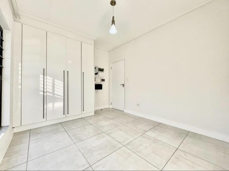 A bright, empty bedroom featuring modern large-format floor tiles and floor-to-ceiling built-in cupboards with a clean, minimalist aesthetic.