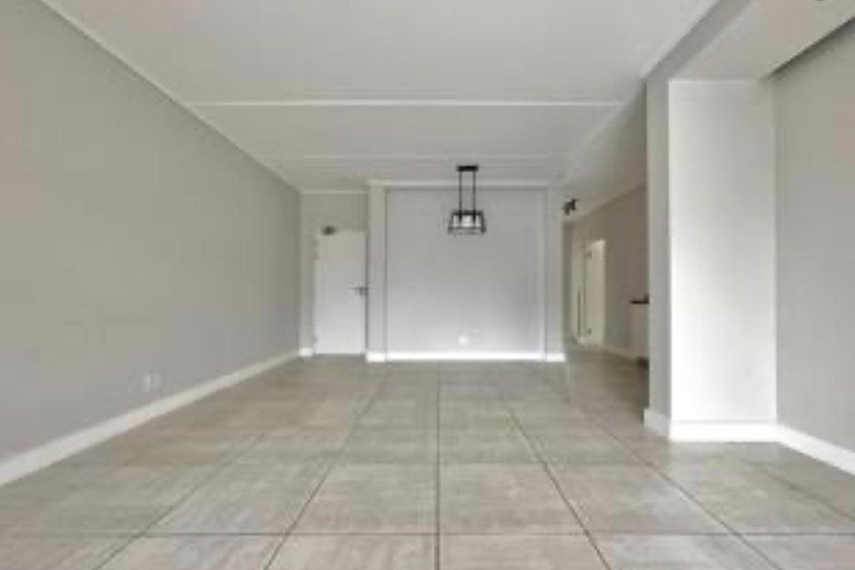 A spacious, empty living area featuring neutral grey walls, large format floor tiles, and a modern pendant light fixture.