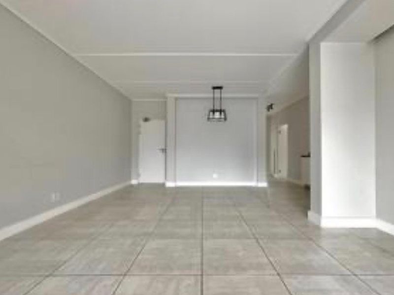 A spacious, empty living area featuring neutral grey walls, large format floor tiles, and a modern pendant light fixture.