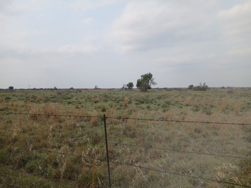 Expansive open farm land featuring natural veld vegetation and a perimeter barbed wire fence.