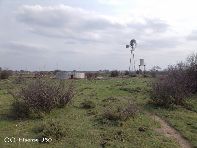 Open farm land featuring a traditional windmill, elevated water tank, and a corrugated steel reservoir for agricultural water storage.