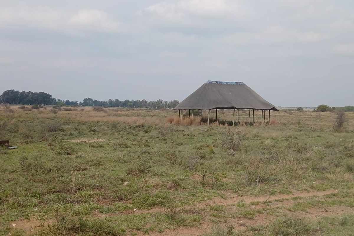 An expansive open field on a farm property featuring a simple, open-sided thatched roof structure in need of maintenance.