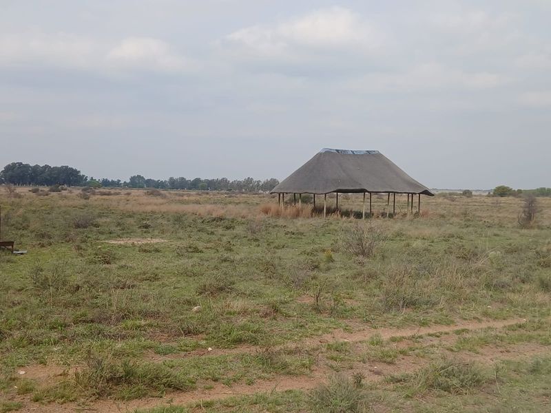 An expansive open field on a farm property featuring a simple, open-sided thatched roof structure in need of maintenance.
