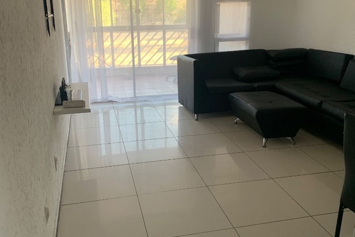 A living room featuring large format floor tiles, a wall-mounted shelf, and a sliding glass door providing access to an outdoor area.