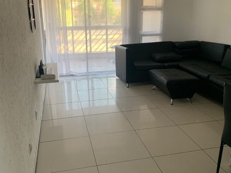 A living room featuring large format floor tiles, a wall-mounted shelf, and a sliding glass door providing access to an outdoor area.