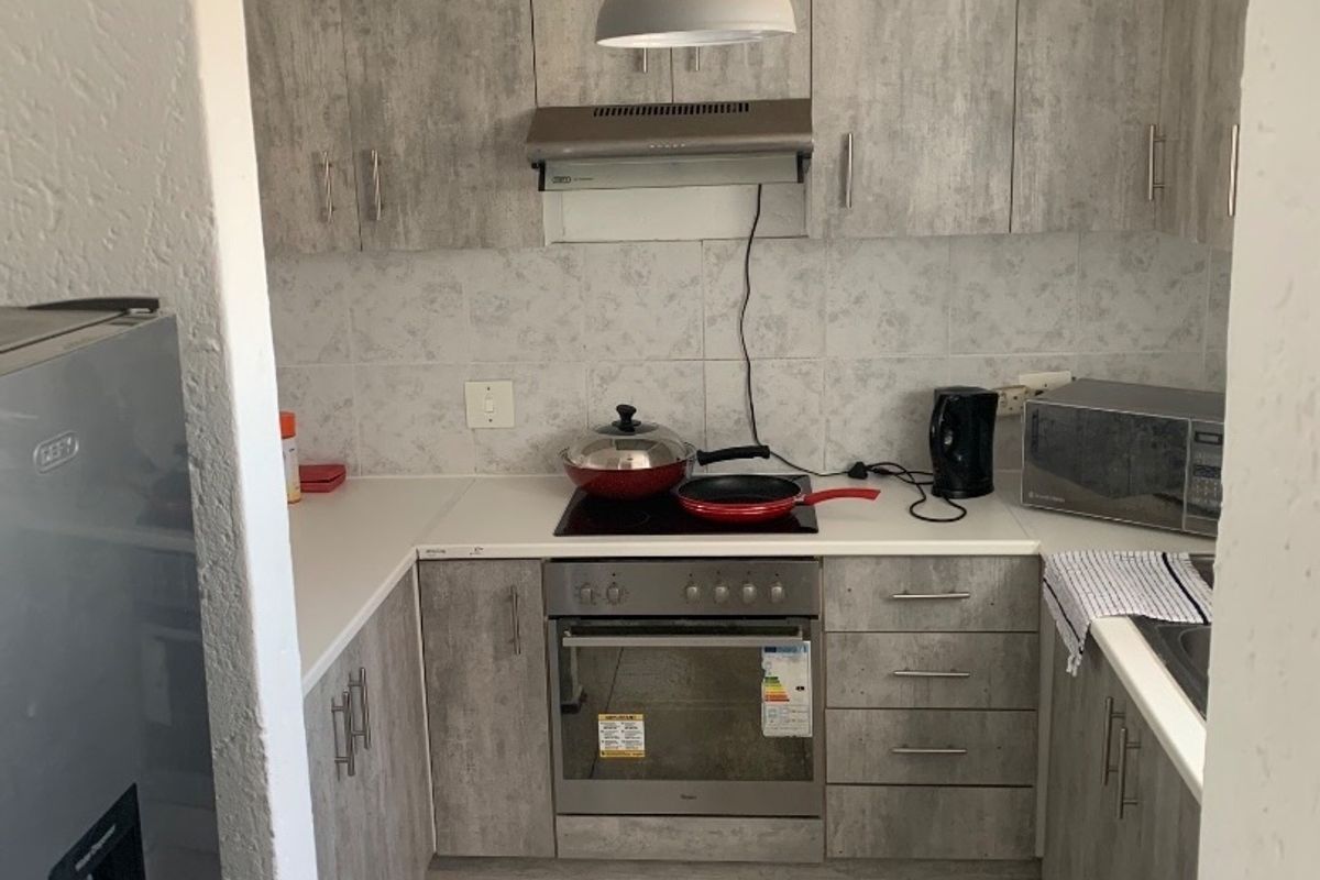 A compact, functional kitchen featuring modern grey wood-look cabinetry, built-in oven and hob, tiled backsplash, and neutral floor tiles.