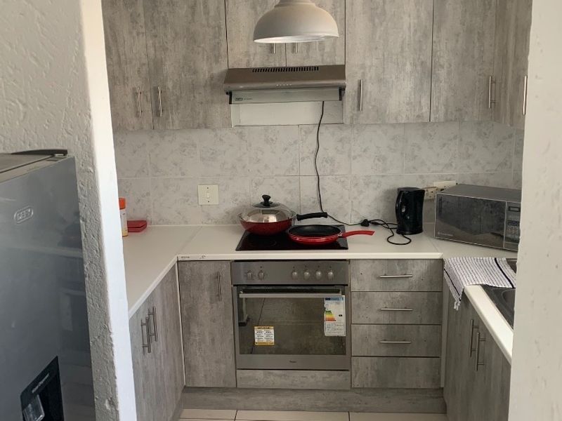 A compact, functional kitchen featuring modern grey wood-look cabinetry, built-in oven and hob, tiled backsplash, and neutral floor tiles.