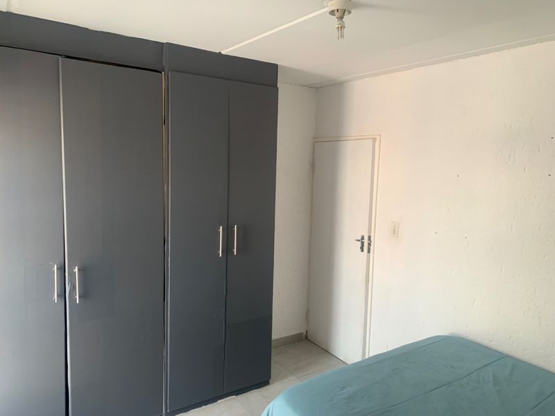 A bedroom featuring built-in dark grey cupboards and tiled flooring, requiring minor cosmetic repairs to the walls and ceiling.