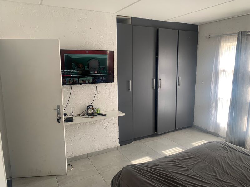 A bedroom featuring tiled flooring, textured walls, and dark grey built-in cupboards providing ample storage space.