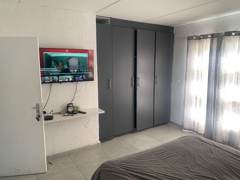A bedroom featuring built-in dark grey cupboards, tiled flooring, and natural light through window curtains.