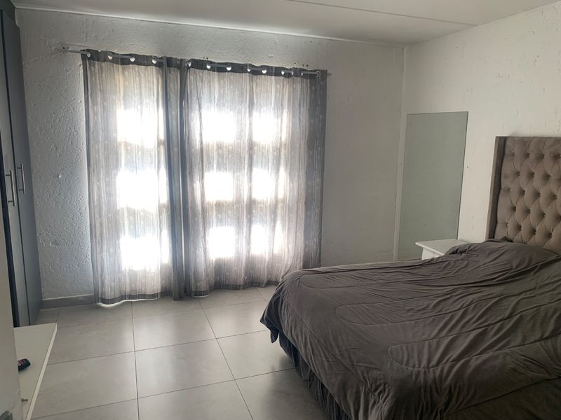 A bedroom featuring tiled flooring and a built-in wardrobe, with natural light filtering through window curtains.