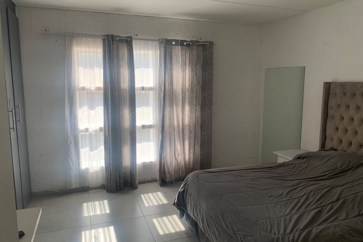 A bedroom featuring tiled flooring, a built-in wardrobe, and natural light through large windows. The room requires cosmetic updates to the wall finishes.