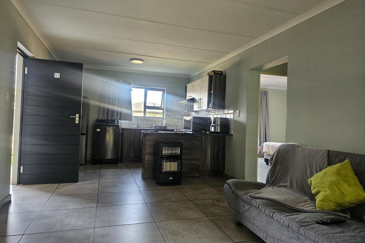 Open plan living area featuring tiled flooring and a functional kitchen with cabinetry, subway tile backsplash, and integrated extractor fan.