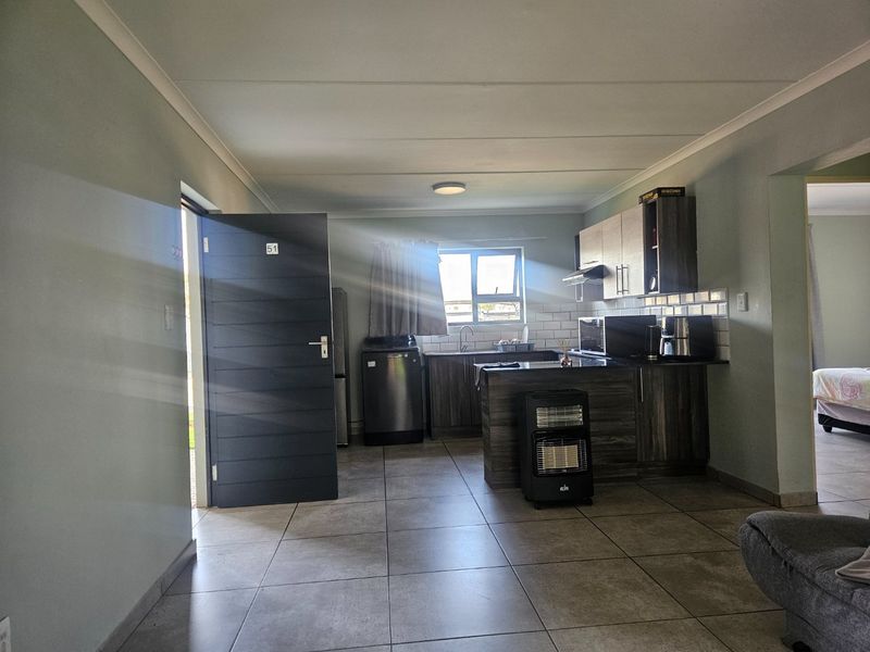 Open-plan kitchen area featuring dark wood-look cabinetry, tiled flooring, and a subway tile backsplash, with direct access to the exterior.