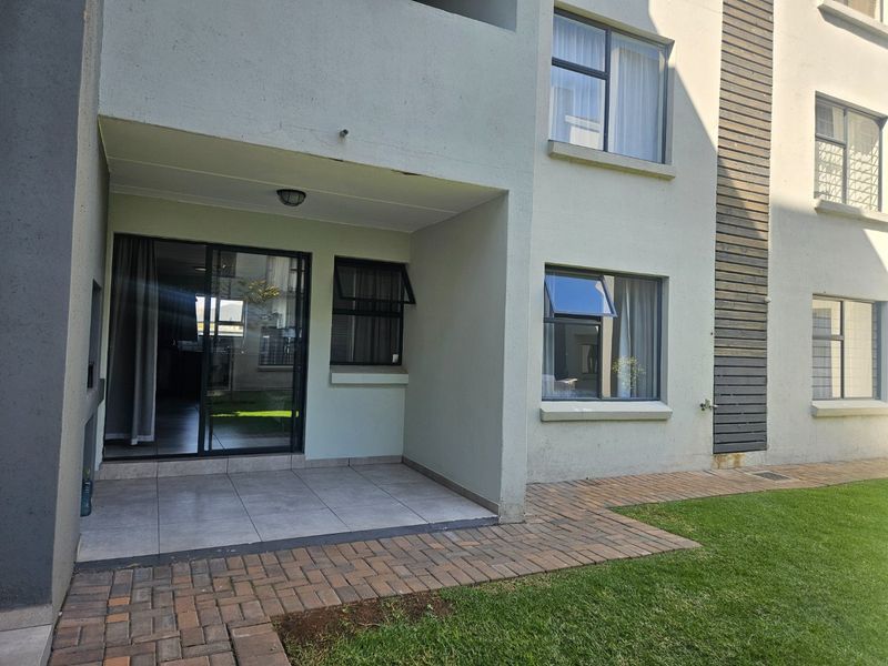 A covered patio area featuring tiled flooring and a sliding glass door, providing direct access to the garden and paved walkway.