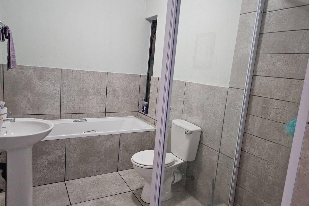 A clean, modern bathroom featuring a pedestal basin, built-in bathtub, toilet, and a separate glass-enclosed shower with neutral grey tiling.