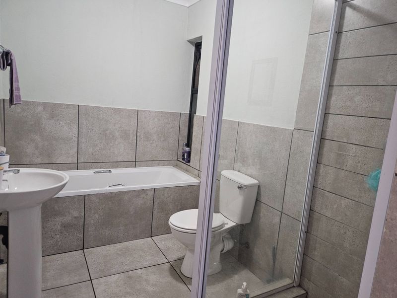 A clean, modern bathroom featuring a pedestal basin, built-in bathtub, toilet, and a separate glass-enclosed shower with neutral grey tiling.