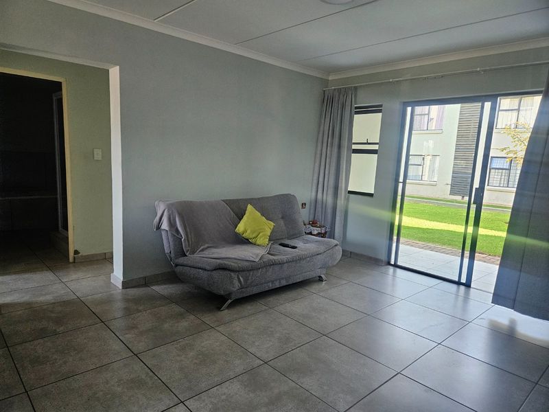 A living room featuring large floor tiles and a sliding glass door providing access to an outdoor area.
