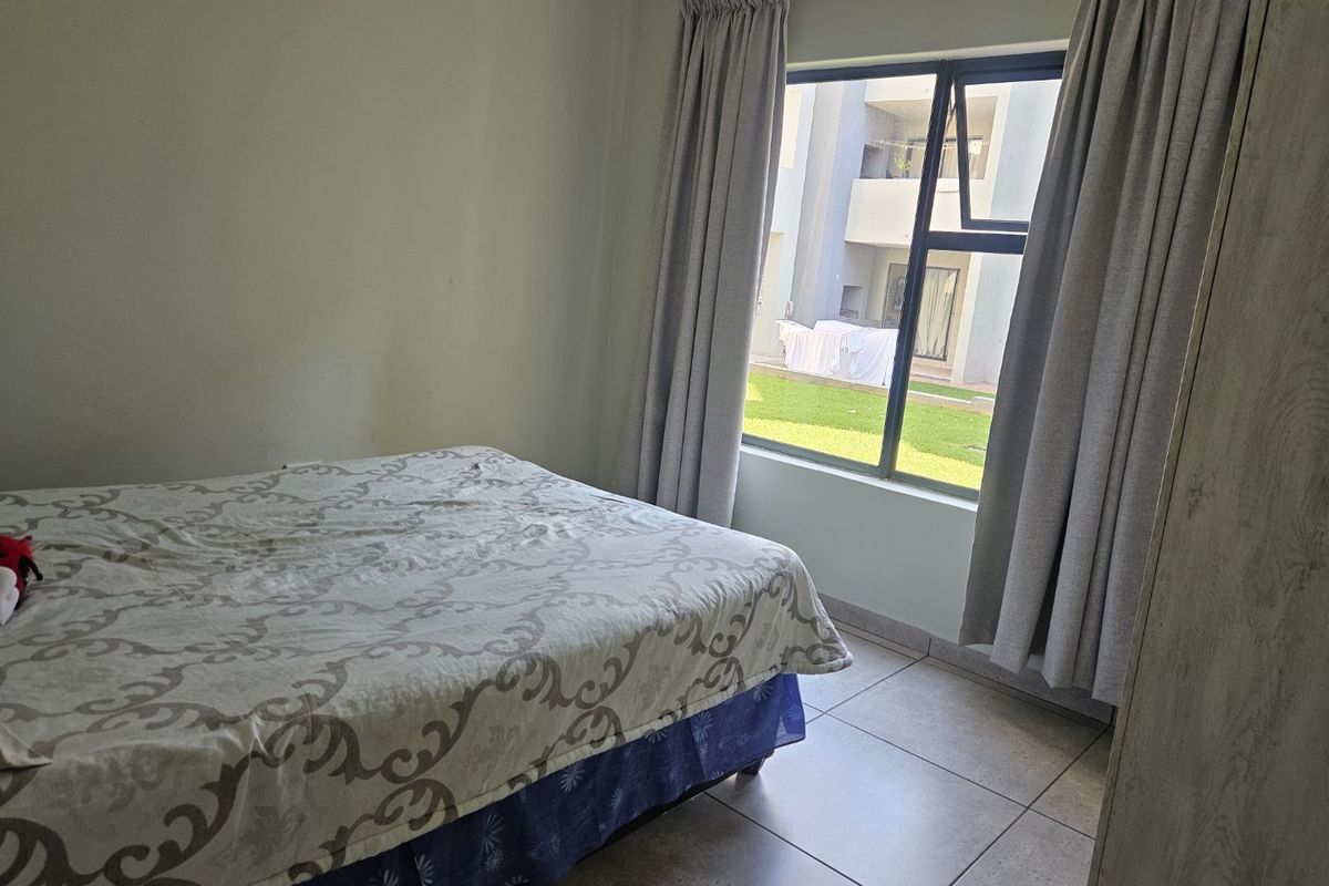 A bedroom featuring tiled flooring and a large window with curtain tracks, offering a view of the apartment complex exterior.