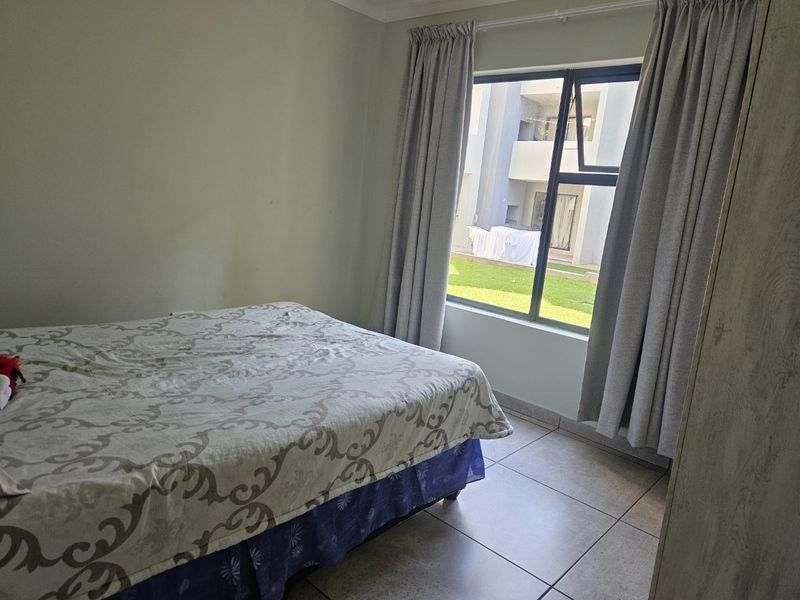 A bedroom featuring tiled flooring and a large window with curtain tracks, offering a view of the apartment complex exterior.