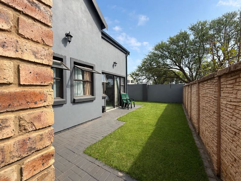 A well-maintained rear garden featuring a paved patio area, a neat lawn, and a secure brick boundary wall.