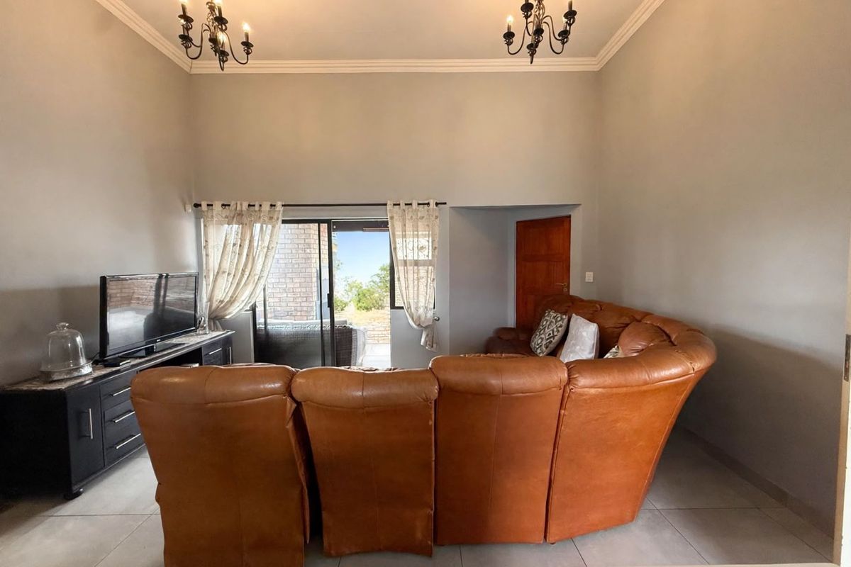 A spacious living room featuring tiled flooring, cove molding, and a sliding glass door providing access to an outdoor patio area.